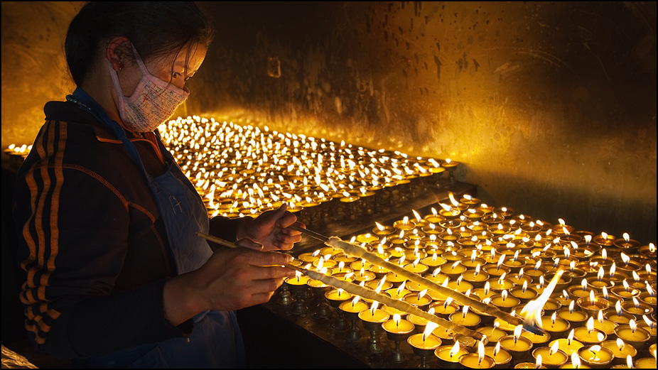 Девушка поправляет свечи в монастыре на Тибете. Фотография Дмитрия Шатрова