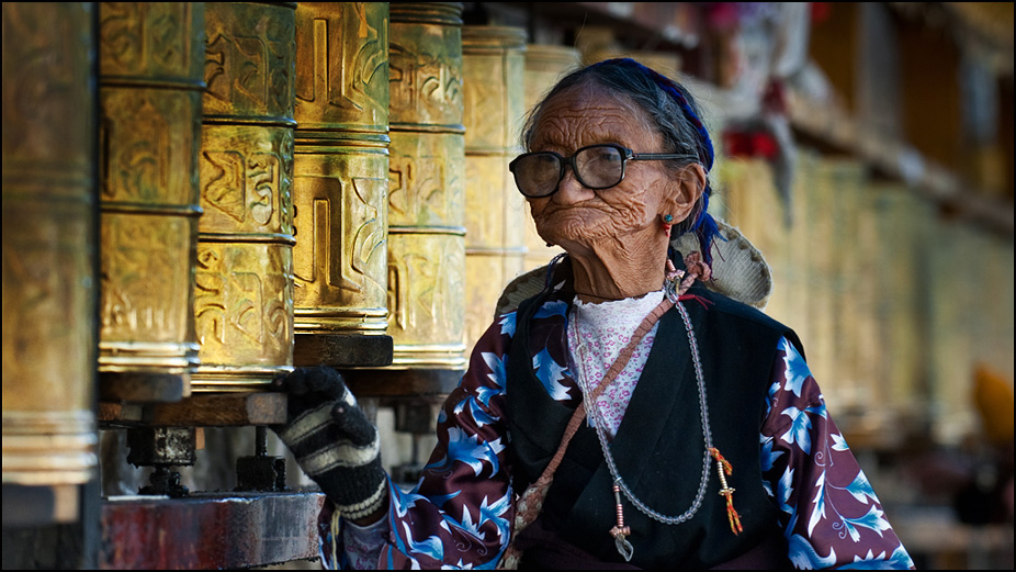 Пожилая женщина крутит молельные барабаны в монастыре на Тибете. Фотография Дмитрия Шатрова